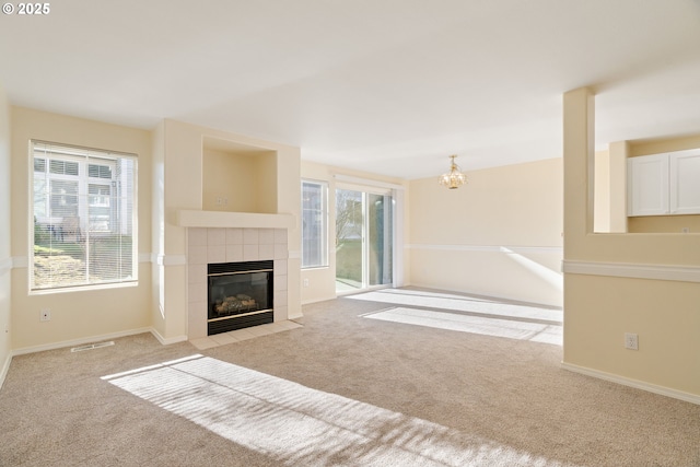 unfurnished living room with an inviting chandelier, a fireplace, and light colored carpet