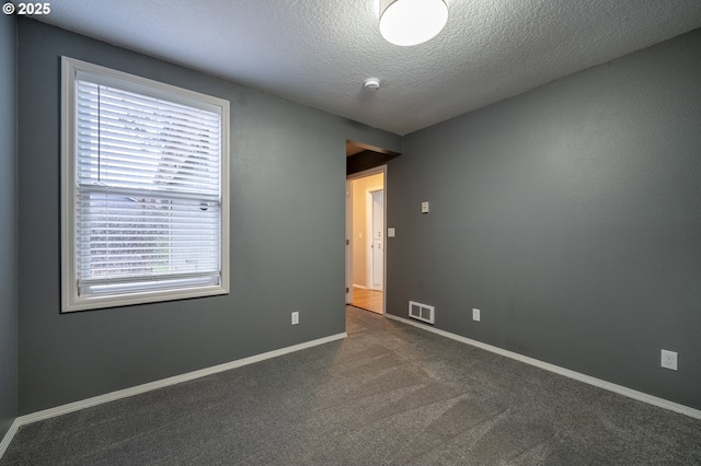 empty room with a textured ceiling, dark carpet, visible vents, and baseboards