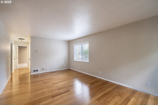 empty room featuring baseboards, visible vents, a textured ceiling, and light wood finished floors