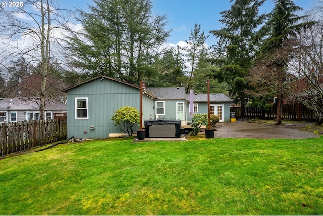 rear view of house with a hot tub, a lawn, a fenced backyard, and a patio