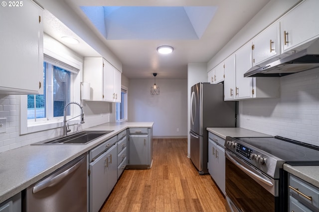 kitchen featuring stainless steel appliances, a sink, white cabinetry, hanging light fixtures, and light countertops