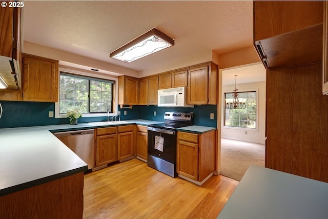 1630 SW 14th St, Warrenton, OR 97146 - kitchen featuring appliances with stainless steel finishes, a chandelier, brown cabinets, light wood-type flooring, and a textured ceiling