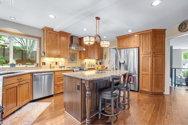 15137 SW Peachtree Dr, Portland, OR 97224 - kitchen featuring stainless steel appliances, wall chimney range hood, light stone counters, light wood-style flooring, and backsplash