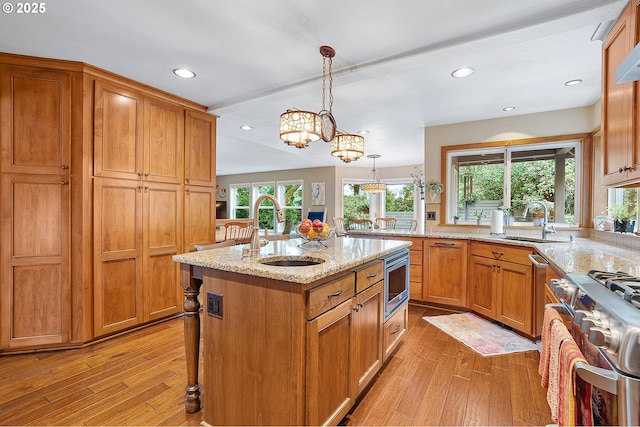 15137 SW Peachtree Dr, Portland, OR 97224 - kitchen featuring appliances with stainless steel finishes, light wood finished floors, recessed lighting, light stone countertops, and a center island with sink