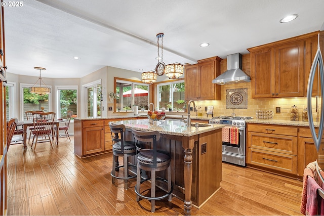 15137 SW Peachtree Dr, Portland, OR 97224 - kitchen featuring stainless steel gas stove, wall chimney range hood, a center island with sink, light wood finished floors, and recessed lighting