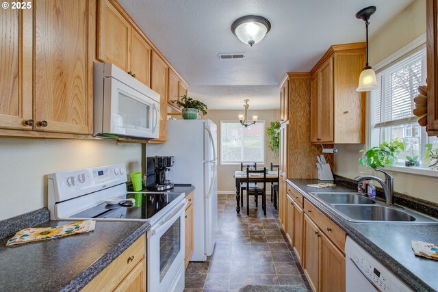 kitchen with dark countertops, visible vents, a notable chandelier, white appliances, and a sink