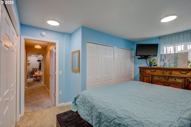 bedroom featuring lofted ceiling, light colored carpet, baseboards, and two closets