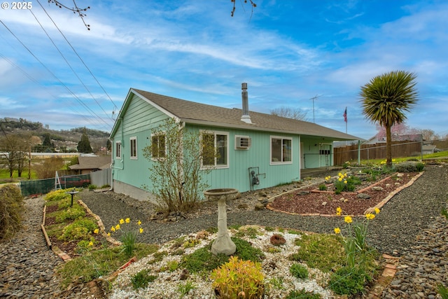 rear view of house featuring a wall unit AC and fence