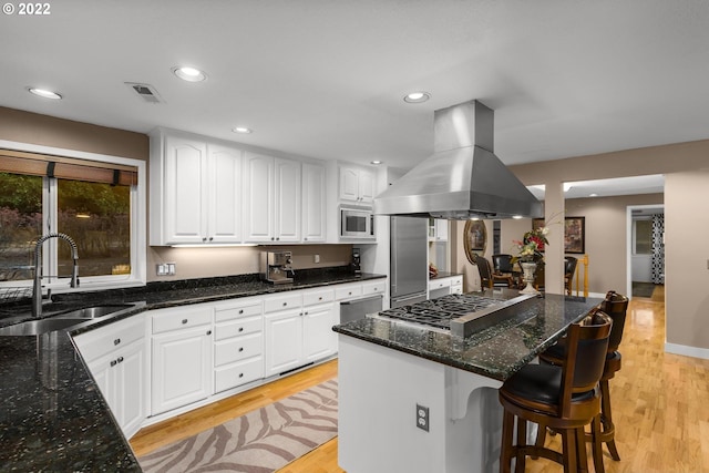 kitchen featuring dark stone counters, stainless steel appliances, island range hood, white cabinetry, and light wood-type flooring