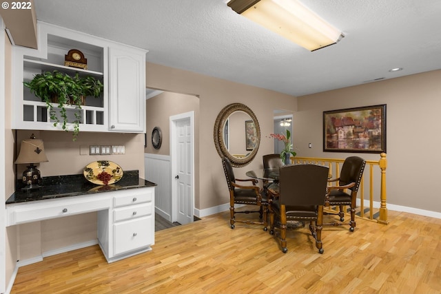 dining space featuring a textured ceiling, built in desk, and light wood-type flooring