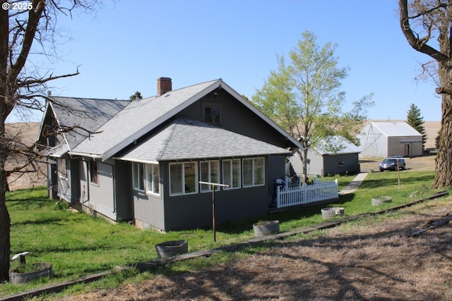 view of home's exterior featuring roof with shingles, a sunroom, a chimney, and a lawn