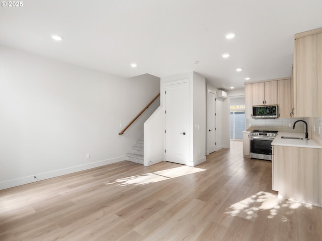 kitchen with baseboards, a sink, appliances with stainless steel finishes, light brown cabinetry, and light wood finished floors