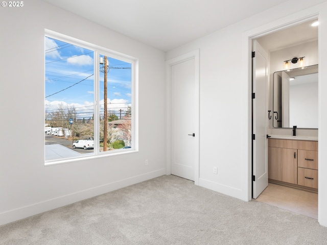 unfurnished bedroom with a sink, light colored carpet, baseboards, and multiple windows
