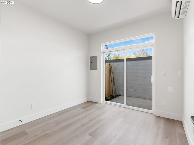 empty room with light wood-style flooring, a wall mounted air conditioner, baseboards, and electric panel