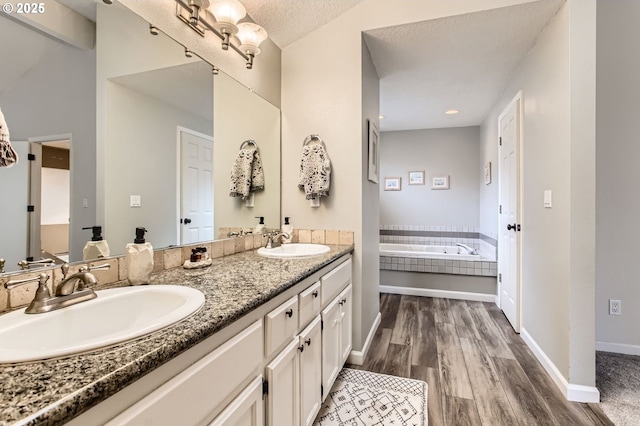 bathroom with double vanity, wood finished floors, a garden tub, and a sink