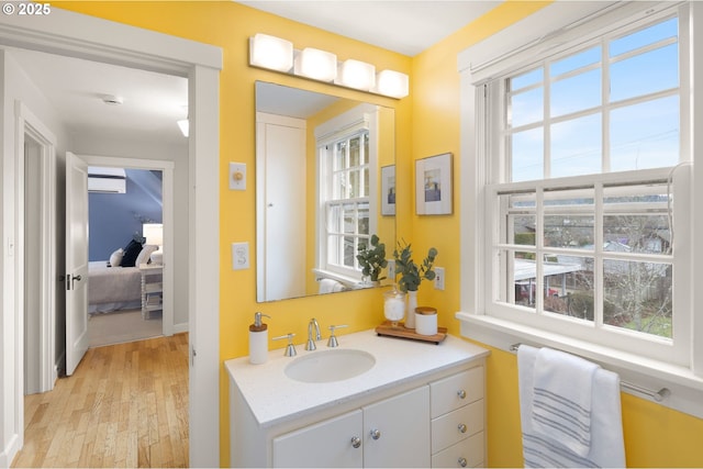 bathroom with vanity, hardwood / wood-style floors, an AC wall unit, and a healthy amount of sunlight