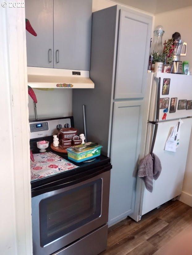 kitchen with stove, white cabinetry, white fridge, and dark wood-type flooring