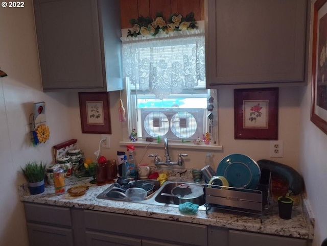 kitchen with gray cabinetry, sink, and light stone counters