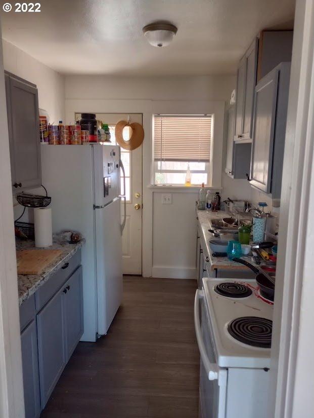 kitchen featuring light stone countertops, stove, white fridge, and dark hardwood / wood-style flooring