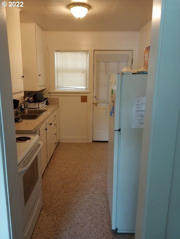 kitchen featuring white cabinets, white appliances, sink, and light carpet