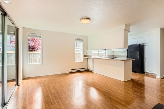 kitchen with plenty of natural light, a baseboard radiator, freestanding refrigerator, and a peninsula