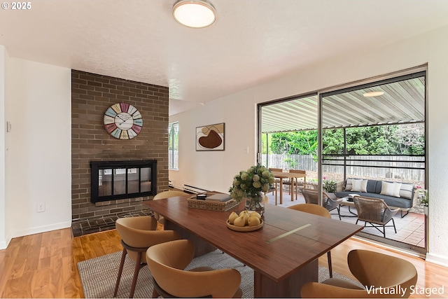 dining space featuring light wood-style floors, baseboards, a fireplace, and a baseboard heating unit