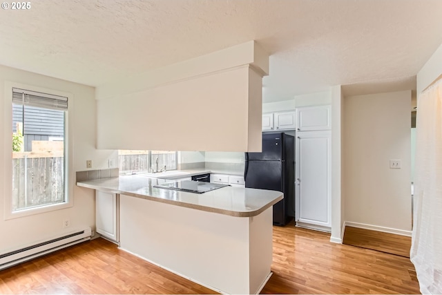 kitchen with baseboard heating, light countertops, black appliances, a peninsula, and light wood-style flooring