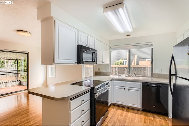 kitchen featuring a peninsula, a wealth of natural light, light wood-style floors, a sink, and black appliances