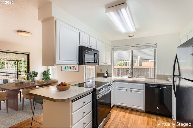 kitchen featuring a sink, light wood finished floors, a peninsula, a healthy amount of sunlight, and black appliances