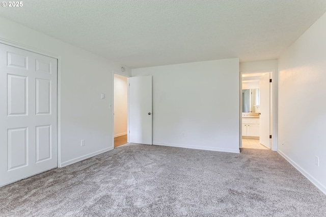unfurnished bedroom featuring baseboards, carpet flooring, a textured ceiling, and ensuite bath