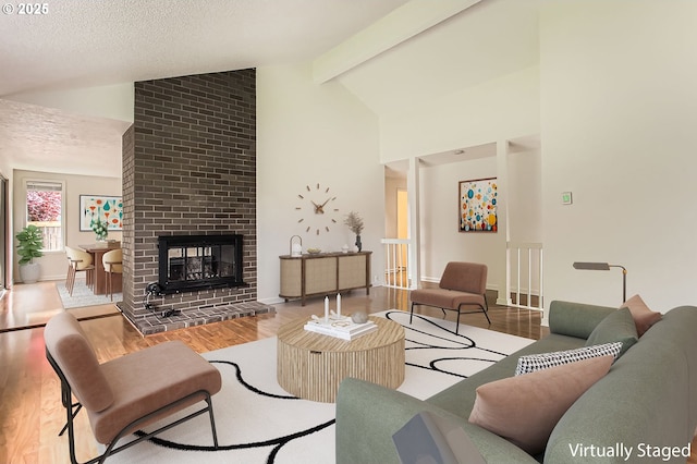 living area featuring a brick fireplace, wood finished floors, beamed ceiling, high vaulted ceiling, and a textured ceiling