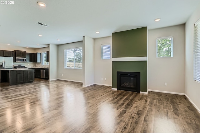 unfurnished living room with a large fireplace, dark wood-style flooring, a wealth of natural light, and baseboards