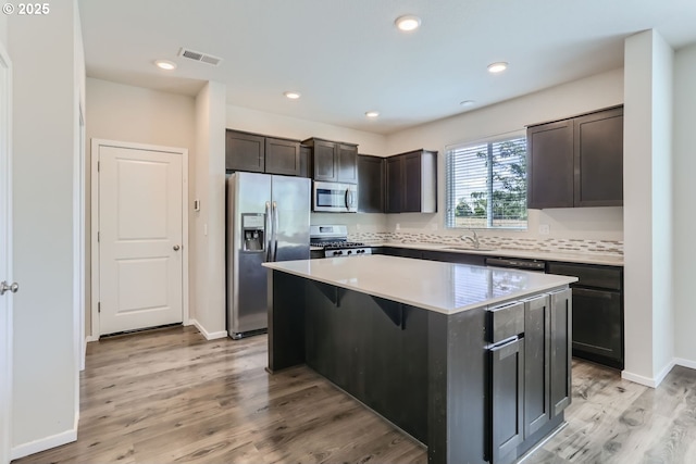 kitchen featuring stainless steel appliances, a sink, a kitchen island, dark brown cabinets, and light wood-type flooring