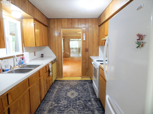 kitchen with white appliances, a healthy amount of sunlight, wooden walls, and sink