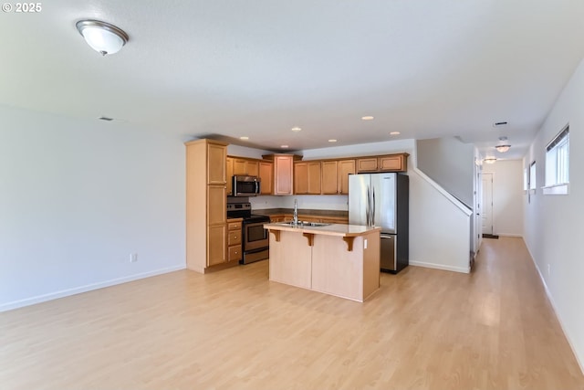 kitchen featuring a kitchen bar, sink, light hardwood / wood-style flooring, appliances with stainless steel finishes, and an island with sink