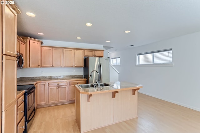 kitchen featuring appliances with stainless steel finishes, sink, a breakfast bar area, a center island with sink, and light hardwood / wood-style flooring