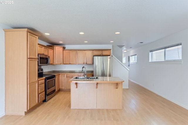 kitchen featuring sink, a kitchen island with sink, stainless steel appliances, a kitchen breakfast bar, and light wood-type flooring