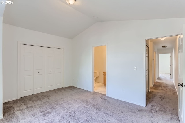 unfurnished bedroom featuring lofted ceiling, light colored carpet, a closet, and ensuite bathroom