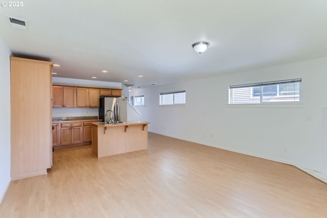 kitchen featuring sink, a breakfast bar area, stainless steel fridge, a kitchen island with sink, and light hardwood / wood-style floors