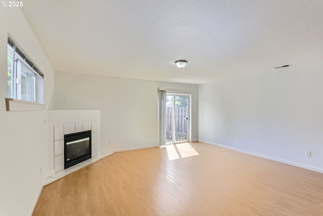 unfurnished living room with a tiled fireplace, light hardwood / wood-style flooring, and a textured ceiling