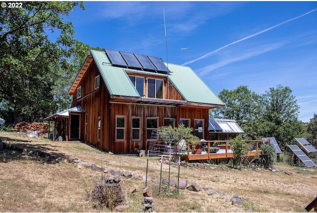 rear view of property featuring a deck and solar panels