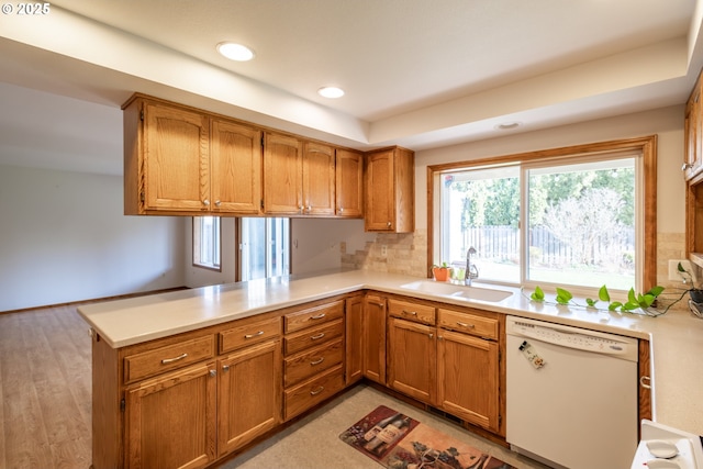 kitchen with white dishwasher, tasteful backsplash, light wood-type flooring, sink, and kitchen peninsula