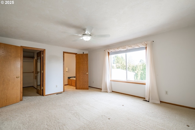 unfurnished bedroom featuring a walk in closet, a textured ceiling, ceiling fan, connected bathroom, and light colored carpet