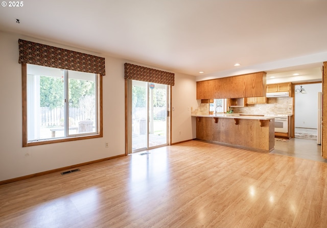 kitchen featuring sink, a breakfast bar, light hardwood / wood-style floors, kitchen peninsula, and decorative backsplash