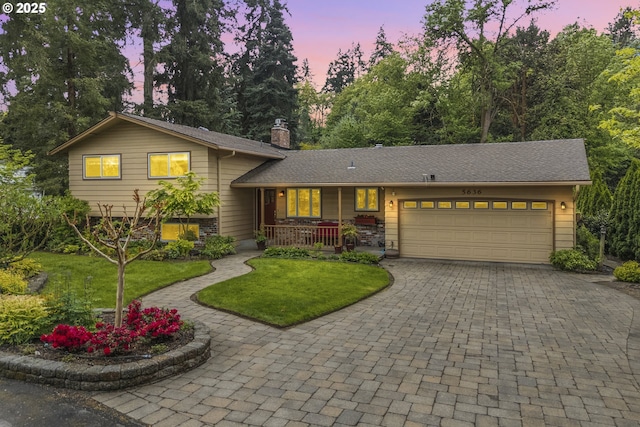 tri-level home featuring covered porch, an attached garage, a front lawn, and decorative driveway