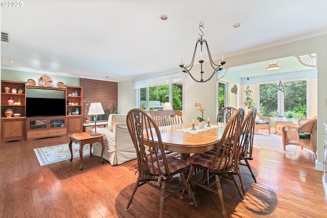 dining space with light wood-type flooring, ornamental molding, visible vents, and an inviting chandelier