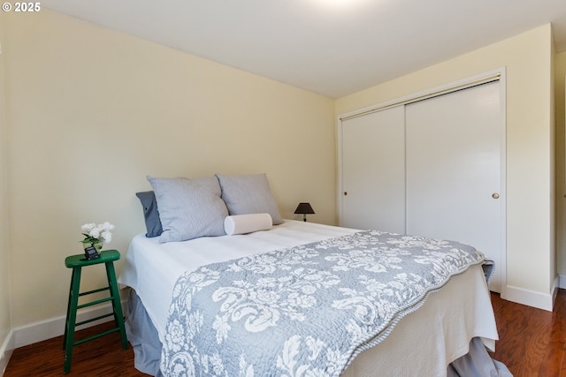 bedroom with baseboards, dark wood-type flooring, and a closet