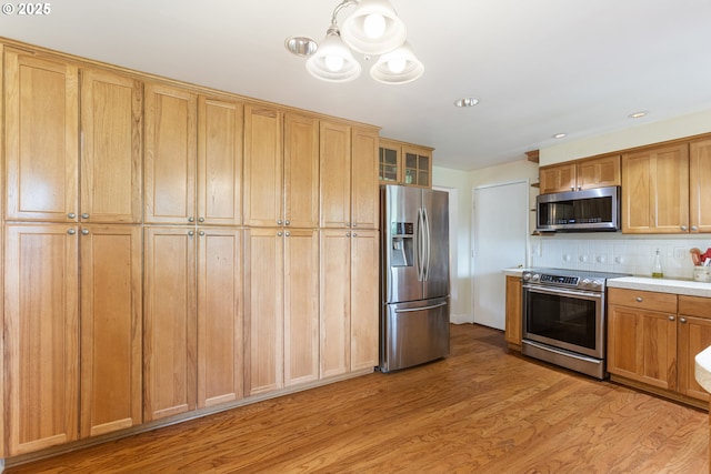 kitchen with decorative backsplash, light countertops, a chandelier, light wood-style floors, and stainless steel appliances