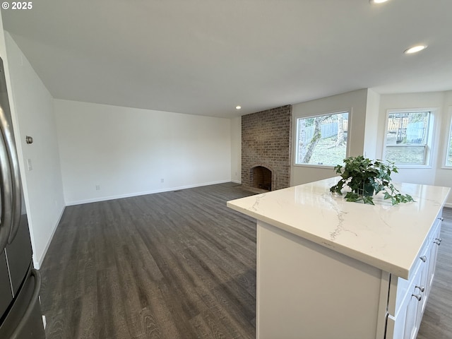 kitchen with white cabinetry, light stone counters, a kitchen island, dark hardwood / wood-style flooring, and a brick fireplace