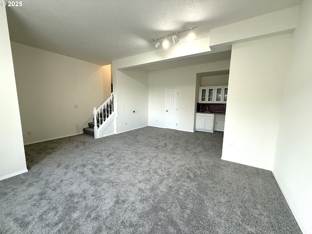 unfurnished living room featuring dark colored carpet, track lighting, and a textured ceiling